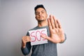 Young handsome man with problem holding banner with sos message over white background with open hand doing stop sign with serious Royalty Free Stock Photo