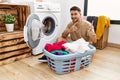 Young handsome man putting dirty laundry into washing machine smiling and looking at the camera pointing with two hands and Royalty Free Stock Photo