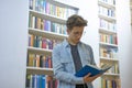 Young handsome man reading a book in a library with big bookshelves in the background Royalty Free Stock Photo