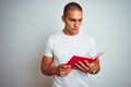 Young handsome man reading red book over white isolated background with a confident expression on smart face thinking serious Royalty Free Stock Photo