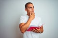 Young handsome man reading red book over white isolated background serious face thinking about question, very confused idea Royalty Free Stock Photo