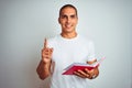 Young handsome man reading red book over white isolated background surprised with an idea or question pointing finger with happy Royalty Free Stock Photo