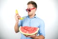 Young handsome man in red eyeglasses with watermelon holding fresh banana like a phone on isolated white background Royalty Free Stock Photo