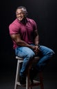 Young handsome man in red shirt and jeans sitting on chair. Athletic muscular male posing for camera on chair. Royalty Free Stock Photo