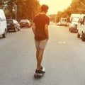 Young handsome man riding a skateboard down the street at sunset. American guy travels around the city in the summer. Royalty Free Stock Photo