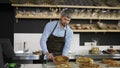 Young handsome man salesman in the apron bringing fresh pies to the counter in the bakery shop. Indoors