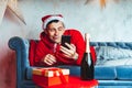 Young handsome man in Santa Claus hat with glass of champagne taking selfie on smartphone. Funny guy photographing himself on