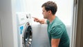 Young handsome man setting washing machine in bathroom. Male doing laundry and housework Royalty Free Stock Photo