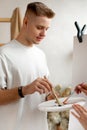 Young handsome man with short fair hair stand holding palette and mixing colors with brush. Art therapy, workshop. Royalty Free Stock Photo