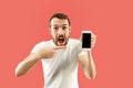 Young handsome man showing smartphone screen isolated on coral background in shock with a surprise face Royalty Free Stock Photo