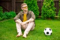 Young handsome man sits on lawn at home with soccer ball on grass, championship Royalty Free Stock Photo