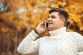 Young handsome man sitting in autumn park and talking by phone. Businessman is calling to someone by smartphone Royalty Free Stock Photo