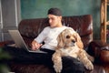 Young handsome man sitting and working at home with his cute dog. Cozy office workplace, remote work, online learning Royalty Free Stock Photo