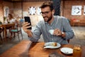 Young handsome man sitting in cafe, enjoying coffee and looking at smartphone. Cafe background Royalty Free Stock Photo