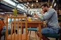 Young handsome man sitting in cafe, listening to music and scroling on the phone. Cafeteria, restaurant, modern architecture