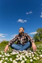 A young handsome man is sitting and having fun in a sunny flower meadow on a sunny day Royalty Free Stock Photo