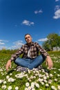 A young handsome man is sitting and having fun in a sunny flower meadow on a sunny day Royalty Free Stock Photo