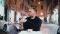 Young handsome man sitting outside in the city cafe and holding smartphone. Male drinking coffee in the evening. Royalty Free Stock Photo