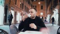 Young handsome man sitting outside in the city cafe and holding smartphone. Male drinking coffee in the evening. Royalty Free Stock Photo