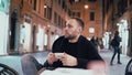 Young handsome man sitting outside in the city cafe and holding smartphone. Male drinking coffee in the evening. Royalty Free Stock Photo