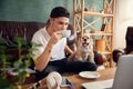 Young handsome man sitting on sofa at home with his cute dog. Cozy office workplace, remote work, online, e-learning Royalty Free Stock Photo