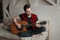 Young handsome man sitting on sofa and playing guitar Royalty Free Stock Photo