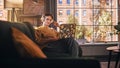 Young Handsome Man Sitting on Sofa Works on Laptop Computer in Sunny Stylish Loft Apartment
