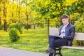 A young handsome man is sitting and working in the park with a laptop. The guy freelancer works outside Royalty Free Stock Photo