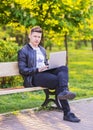 A young handsome man is sitting and working in the park with a laptop. The guy freelancer works outside Royalty Free Stock Photo