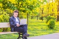 A young handsome man is sitting and working in the park with a laptop. The guy freelancer works outside Royalty Free Stock Photo