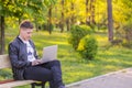 A young handsome man is sitting and working in the park with a laptop. The guy freelancer works outside Royalty Free Stock Photo