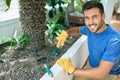 Young handsome man smiling happy caring plants using garden shovel at terrace