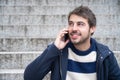 Young handsome man, smiling, talking on the phone sitting on the stairs. Royalty Free Stock Photo