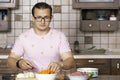 Young handsome man squints from fresh cut onion during cooking process at wooden home kitchen in classical style. Vegetables and r Royalty Free Stock Photo