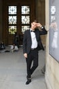 Young handsome man standing and leaning on building, wearing black suit and bow tie. Royalty Free Stock Photo