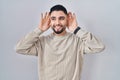 Young handsome man standing over isolated background trying to hear both hands on ear gesture, curious for gossip Royalty Free Stock Photo