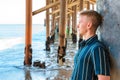 Young handsome man stands under a wooden pier on Malibu beach, California Royalty Free Stock Photo