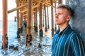 Young handsome man stands under a wooden pier on Malibu beach, California Royalty Free Stock Photo