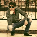 Young handsome man in sunglasses sitting on sidewalk Royalty Free Stock Photo