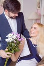 Young handsome man surprising her beautiful girlfriend and gives her bouquet of purple white flowers. Royalty Free Stock Photo