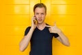 Young handsome man talking on mobile phone and pointing finger in front of yellow door Royalty Free Stock Photo