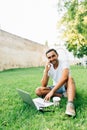 Young handsome man talking on the phone while working on laptop on the grass in park Royalty Free Stock Photo