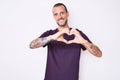 Young handsome man with tattoo wearing casual clothes smiling in love doing heart symbol shape with hands