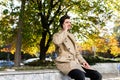 Young handsome man in trench coat joyfully talking on cellphone outdoor