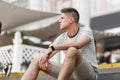 Young handsome man with trendy hairstyle in a stylish striped t-shirt in fashionable beige shorts sits on the stairs in the city Royalty Free Stock Photo