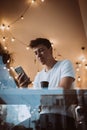 Young, handsome man uses a smartphone in a cafe. Photo behind glass