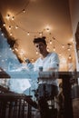 Young, handsome man uses a smartphone in a cafe. Photo behind glass