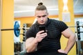 Young handsome man using phone while having exercise break in gym. Royalty Free Stock Photo