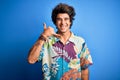 Young handsome man on vacation wearing summer shirt over isolated blue background smiling doing phone gesture with hand and Royalty Free Stock Photo