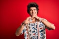 Young handsome man on vacation wearing summer shirt over isolated red background smiling in love doing heart symbol shape with Royalty Free Stock Photo